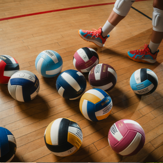 Colorful volleyballs on a wooden floor with a person's feet in the background