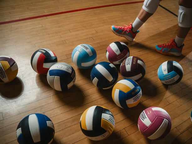 Colorful volleyballs on a wooden floor with a person's feet in the background