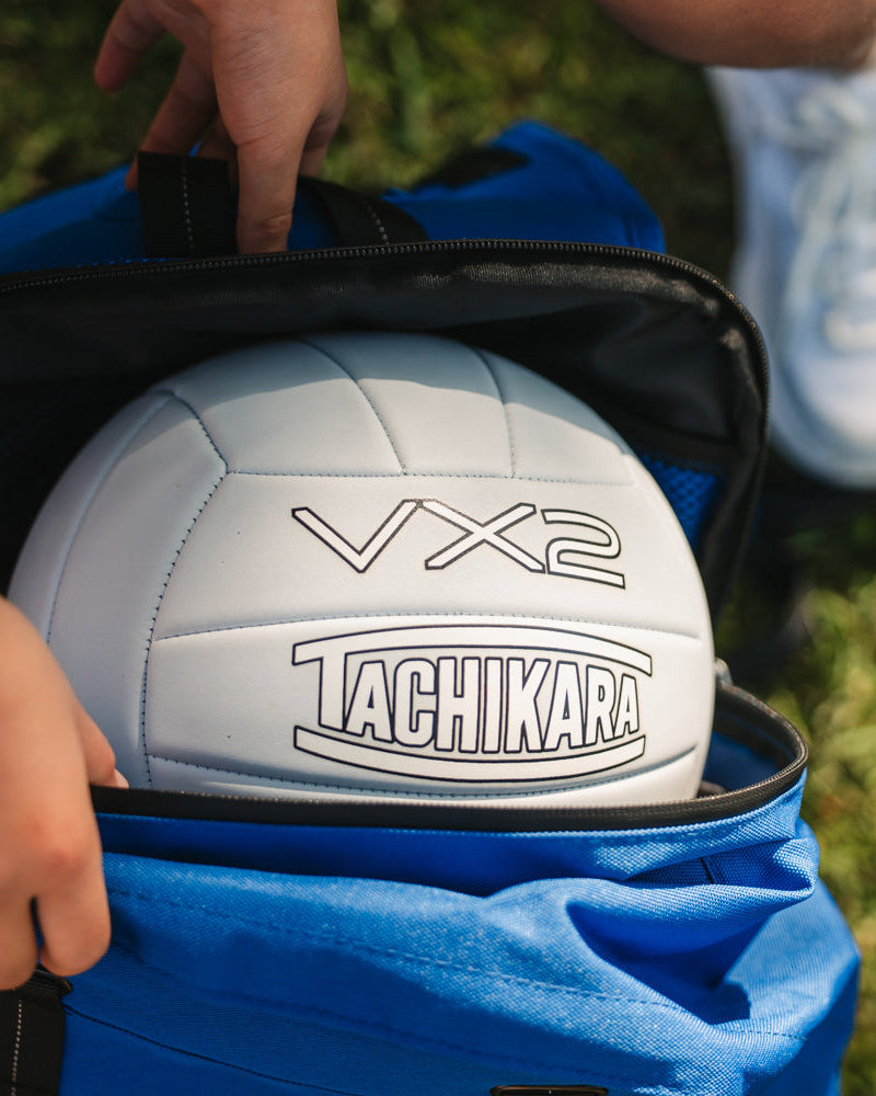Tachikara VX2 volleyball being placed into a blue bag on grass.